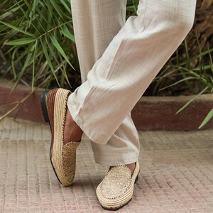 Puede incluir: Un par de mocasines de paja trenzada con ribetes de cuero marr&oacute;n. Los mocasines los lleva una persona que lleva pantalones beige.