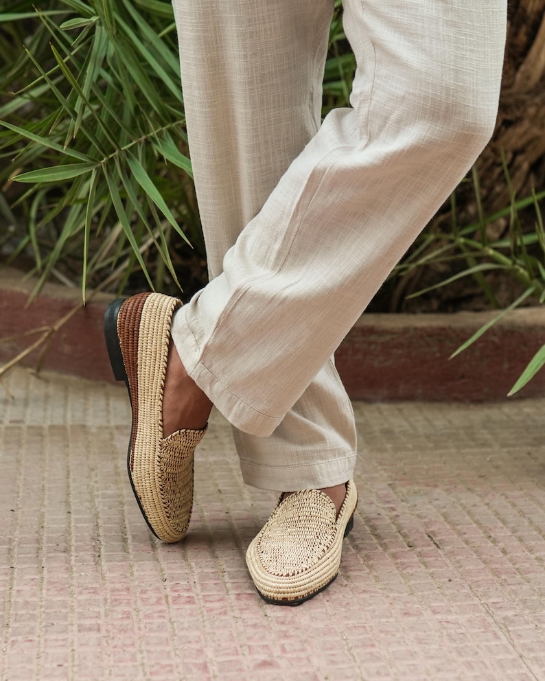 Puede incluir: Un par de mocasines de paja trenzada con ribetes de cuero marr&oacute;n. Los mocasines los lleva una persona que lleva pantalones beige.