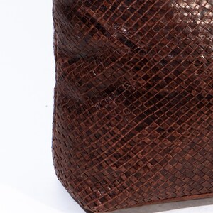 Puede incluir: Primer plano de un bolso tote de cuero marr&oacute;n con un patr&oacute;n tejido. El bolso tiene una superficie lisa y texturizada.