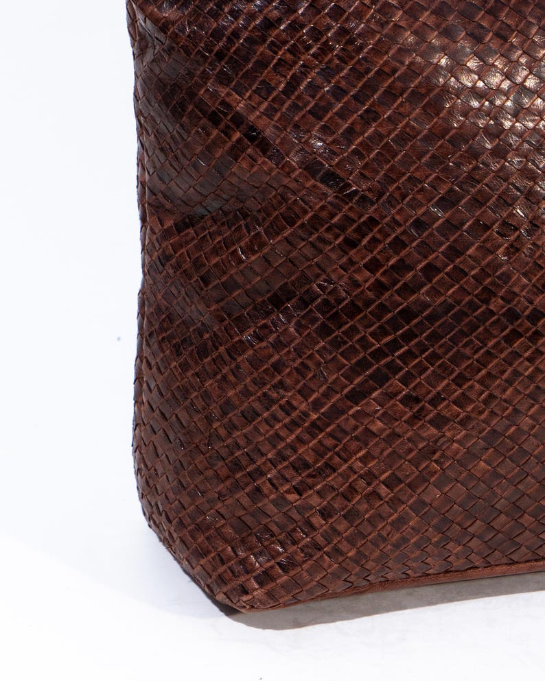 Puede incluir: Primer plano de un bolso tote de cuero marr&oacute;n con un patr&oacute;n tejido. El bolso tiene una superficie lisa y texturizada.
