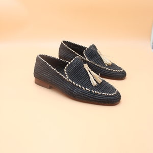 K&ouml;nnte beinhalten: Ein Paar schwarze geflochtene Lederschuhe mit Quaste. Die Schuhe haben einen wei&szlig;en Steppdetail an den R&auml;ndern.