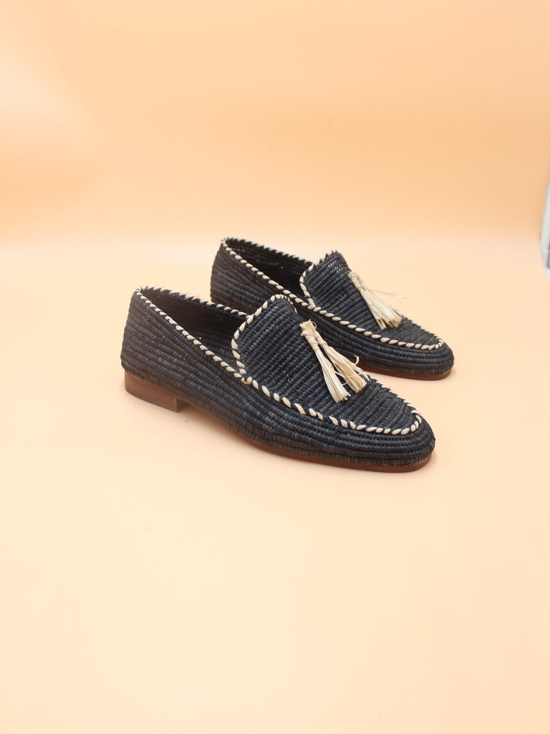 K&ouml;nnte beinhalten: Ein Paar schwarze geflochtene Lederschuhe mit Quaste. Die Schuhe haben einen wei&szlig;en Steppdetail an den R&auml;ndern.