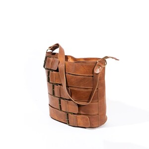 Pu&ograve; includere: Una borsa a tracolla in pelle marrone con pi&ugrave; fibbie e una lunga tracolla.