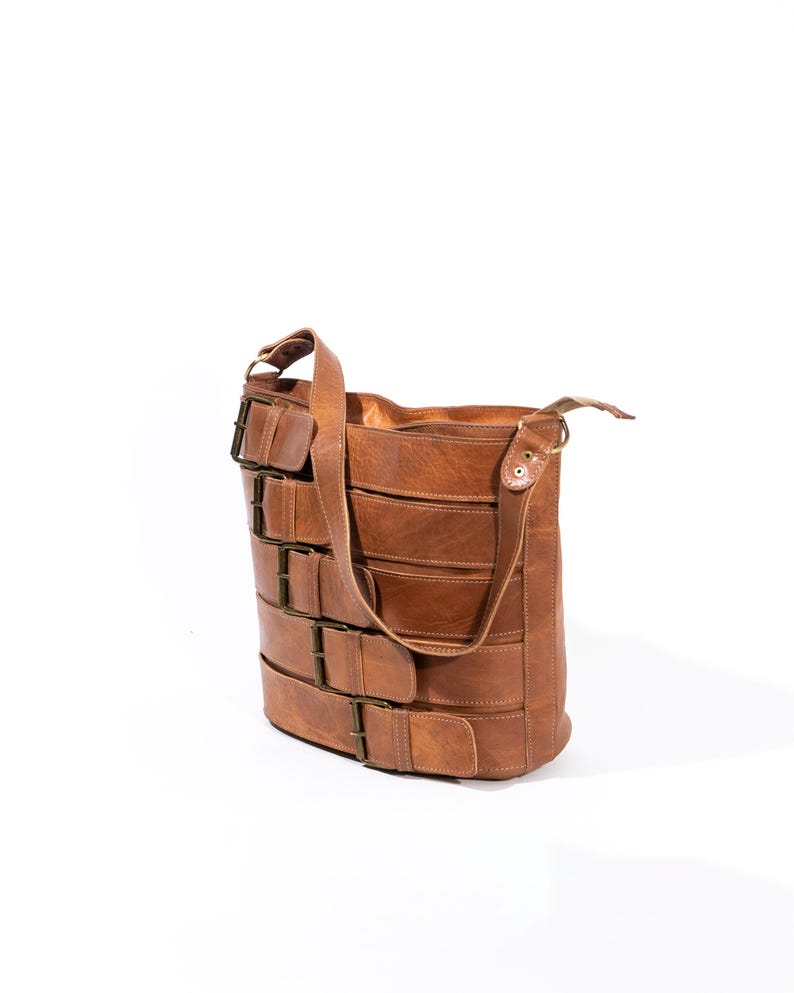 Pu&ograve; includere: Una borsa a tracolla in pelle marrone con pi&ugrave; fibbie e una lunga tracolla.