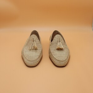 May include: A pair of beige woven leather loafers with tassels. The loafers are on a light orange background.