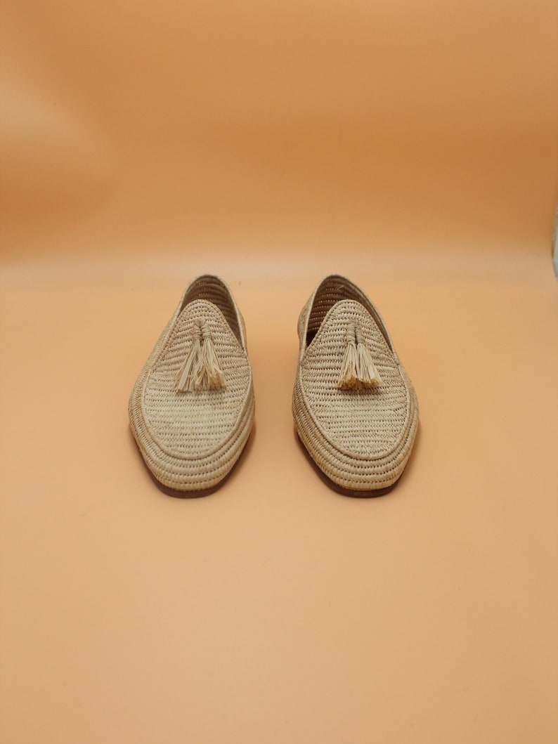 May include: A pair of beige woven leather loafers with tassels. The loafers are on a light orange background.