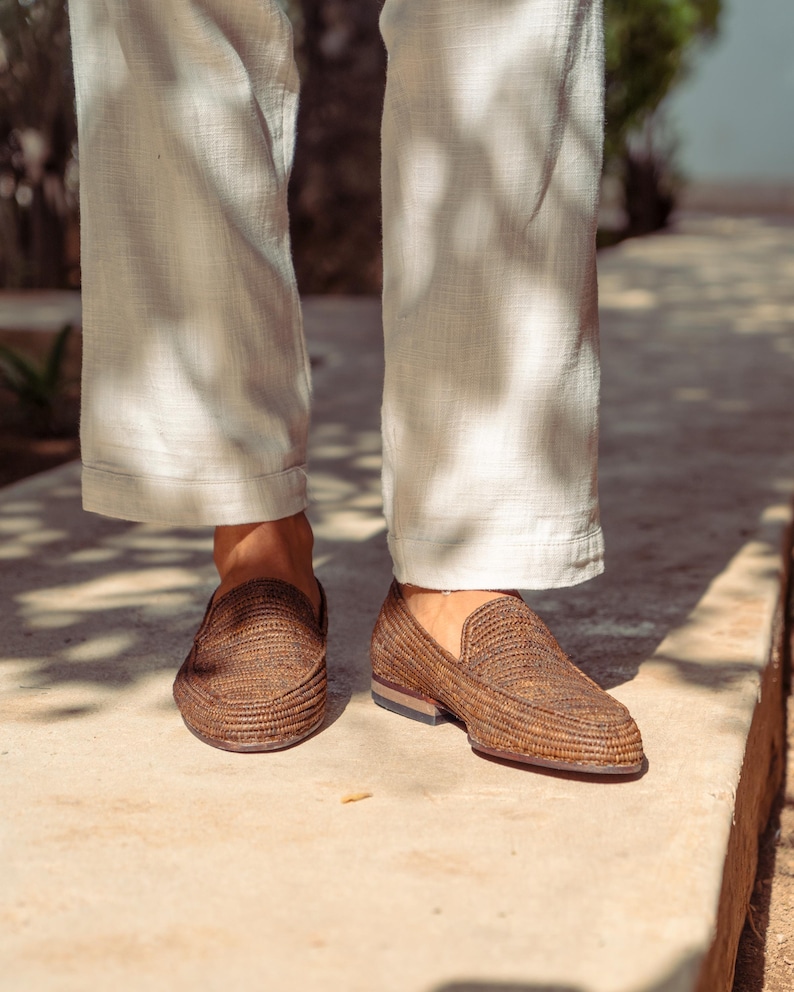 K&ouml;nnte beinhalten: Ein Paar braune geflochtene Lederschuhe mit dezenter Textur. Die Schuhe werden von einer Person getragen, die eine wei&szlig;e Hose tr&auml;gt.