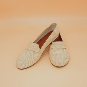 May include: A pair of cream-colored woven straw slip-on shoes with a pointed toe.