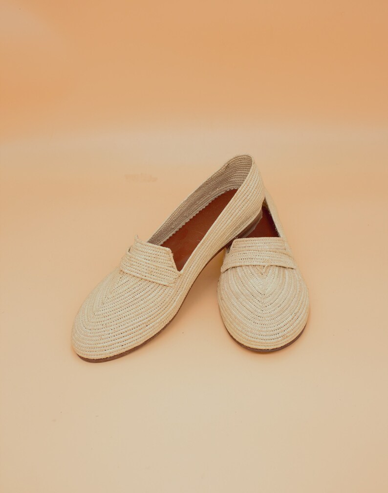 May include: A pair of cream-colored woven straw slip-on shoes with a pointed toe.