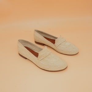 May include: A pair of cream-colored woven straw loafers. The loafers have a pointed toe and a flat sole.