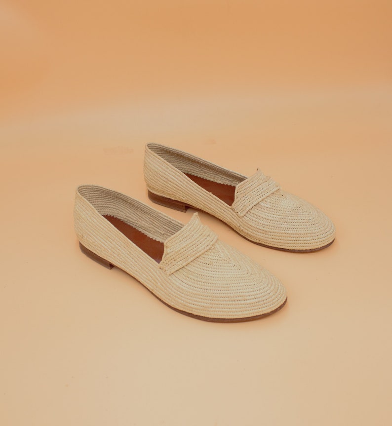 May include: A pair of cream-colored woven straw loafers. The loafers have a pointed toe and a flat sole.