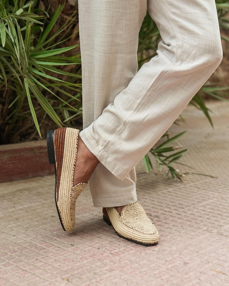 Puede incluir: Un par de mocasines de paja trenzada con detalles de cuero marr&oacute;n. Los mocasines los lleva puestos una persona de pie sobre un suelo de baldosas.