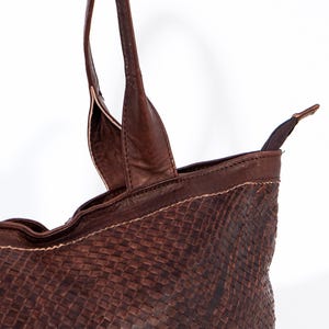 Puede incluir: Un bolso tote de cuero marr&oacute;n con un patr&oacute;n tejido. El bolso tiene dos asas superiores y un cierre de cremallera.