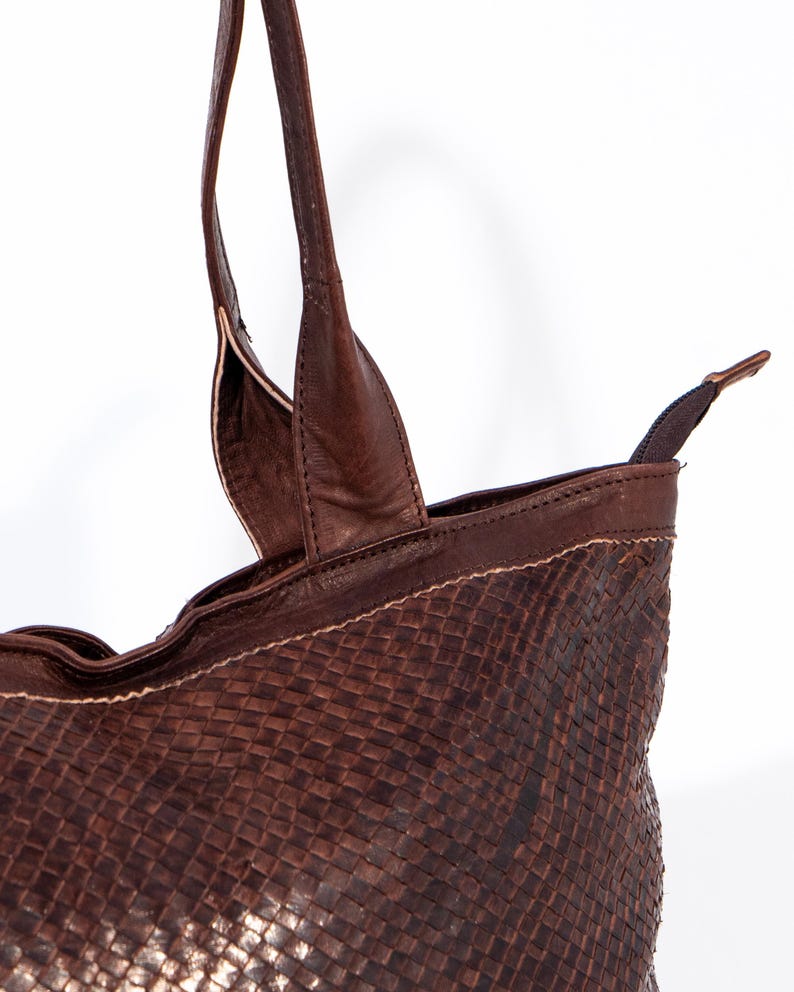 Puede incluir: Un bolso tote de cuero marr&oacute;n con un patr&oacute;n tejido. El bolso tiene dos asas superiores y un cierre de cremallera.