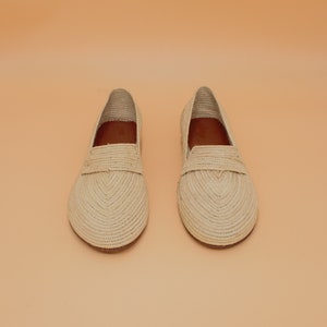 May include: A pair of beige woven leather loafers. The loafers have a pointed toe and a flat sole.