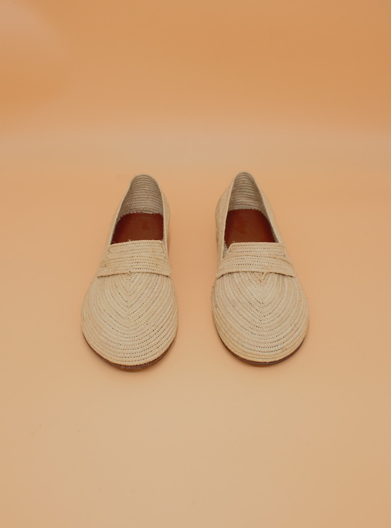 May include: A pair of beige woven leather loafers. The loafers have a pointed toe and a flat sole.