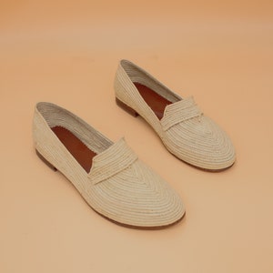 May include: A pair of cream-colored woven straw loafers. The loafers have a rounded toe and a flat sole.