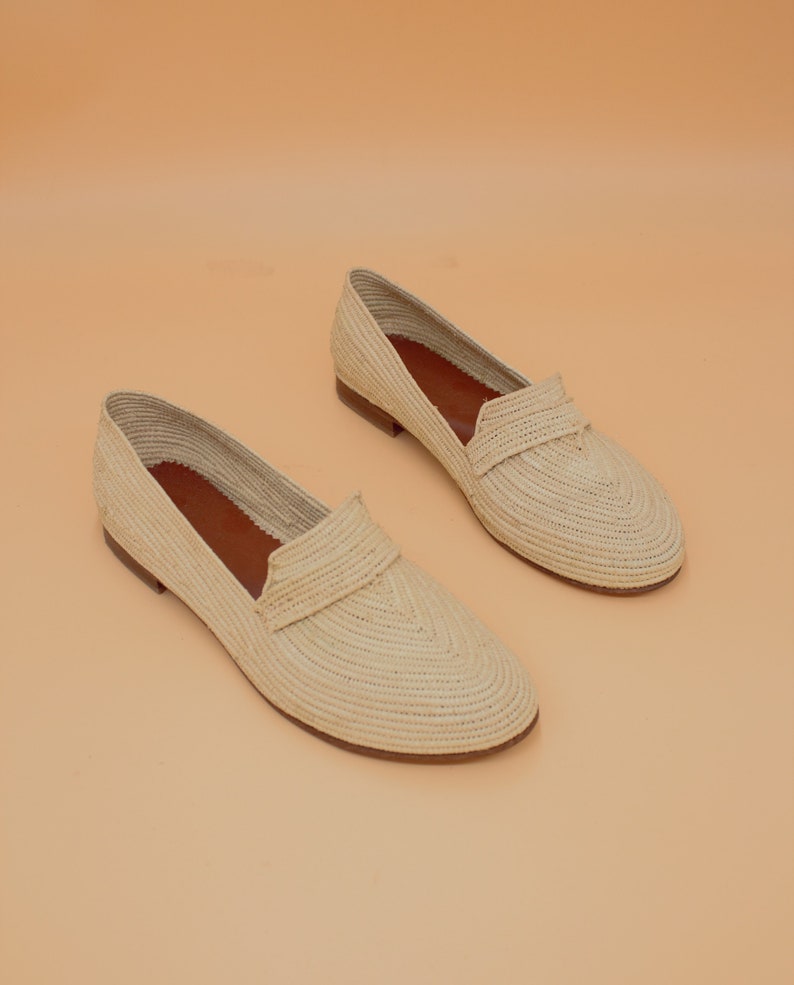 May include: A pair of cream-colored woven straw loafers. The loafers have a rounded toe and a flat sole.