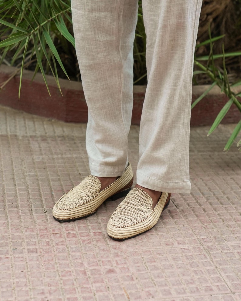 Puede incluir: Un par de mocasines de paja trenzada con ribete de cuero marr&oacute;n. Los mocasines se llevan con pantalones de lino beige claro.