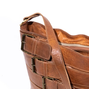 Pu&ograve; includere: Una borsa tote in pelle marrone con pi&ugrave; fibbie e una lunga tracolla. La borsa ha una chiusura a zip e una texture morbida e flessibile.