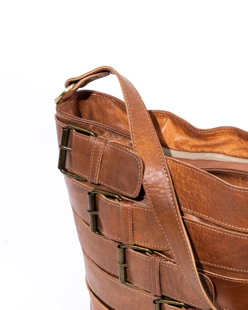 Pu&ograve; includere: Una borsa tote in pelle marrone con pi&ugrave; fibbie e una lunga tracolla. La borsa ha una chiusura a zip e una texture morbida e flessibile.