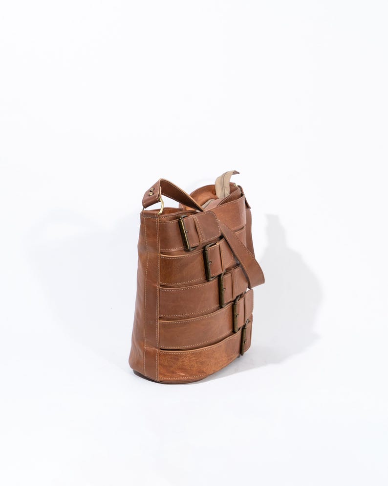 Pu&ograve; includere: Una borsa a tracolla in pelle marrone con pi&ugrave; fibbie. La borsa ha una tracolla lunga e una chiusura a lembo.