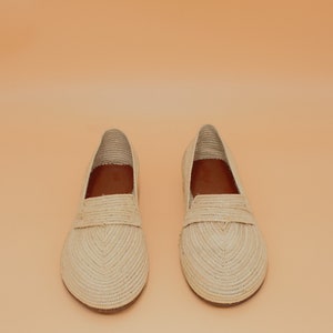 May include: A pair of beige woven leather loafers. The loafers have a simple design with a rounded toe and a flat sole.