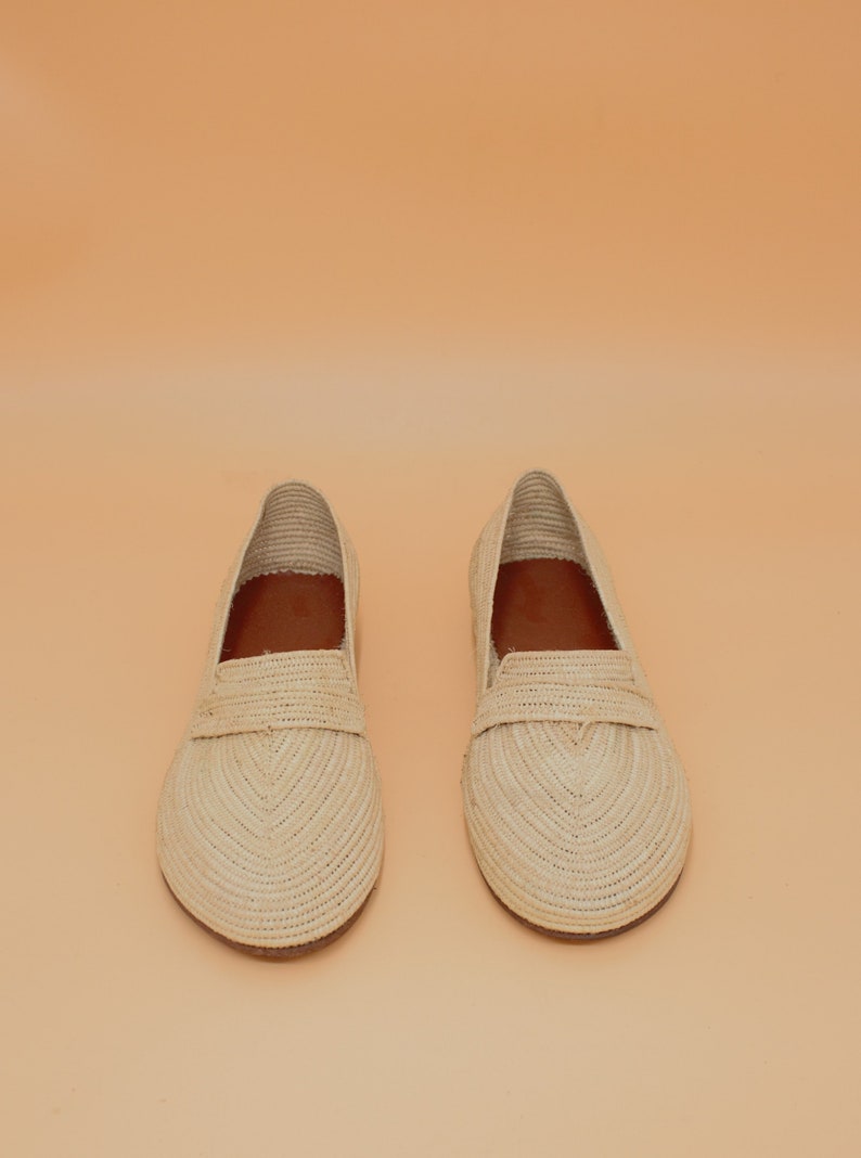 May include: A pair of beige woven leather loafers. The loafers have a simple design with a rounded toe and a flat sole.