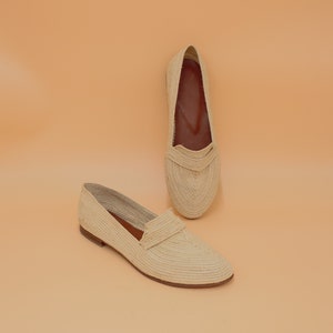 May include: A pair of cream-colored woven straw flats. The shoes have a pointed toe and a flat sole.