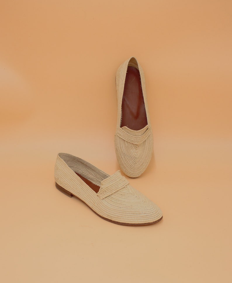 May include: A pair of cream-colored woven straw flats. The shoes have a pointed toe and a flat sole.