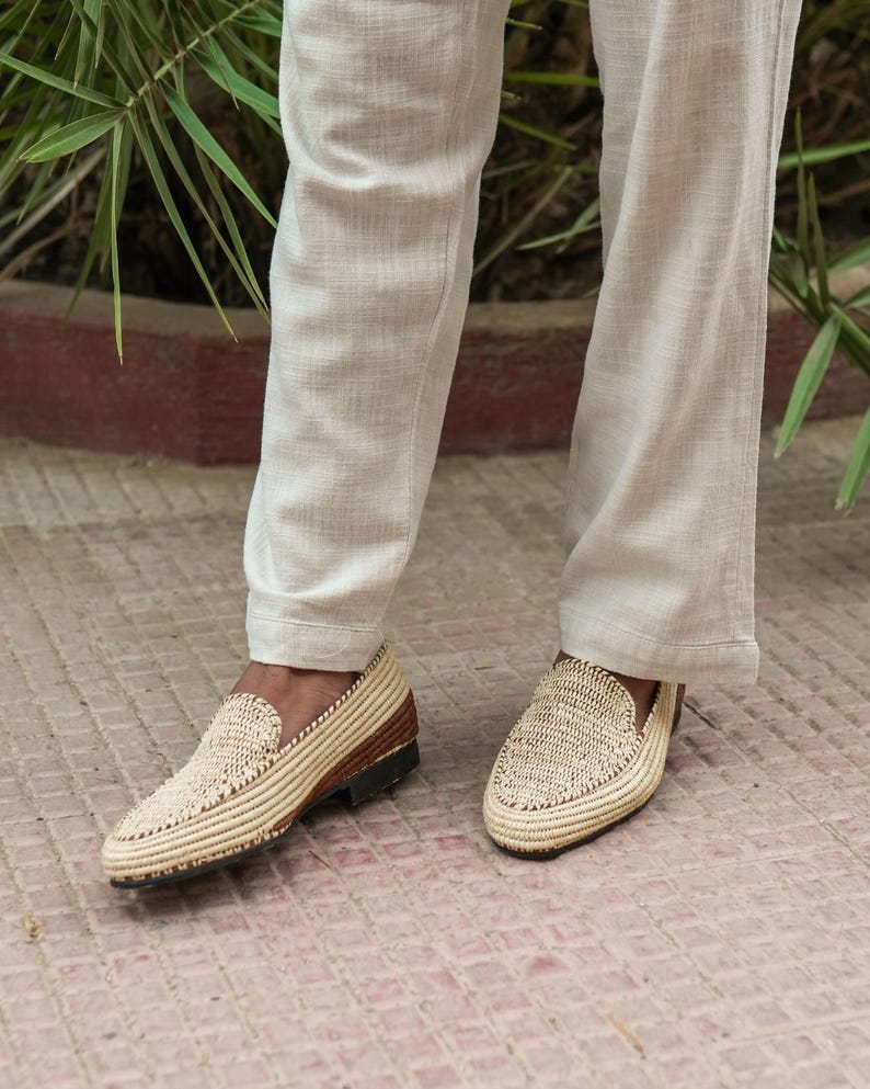Puede incluir: Un par de mocasines de paja trenzada con suelas de cuero marr&oacute;n. Los mocasines son usados por una persona que lleva pantalones de color claro.