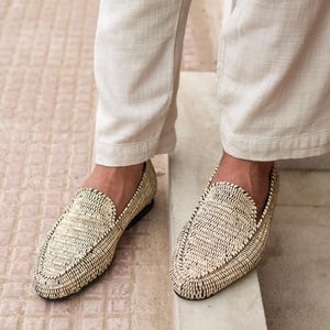 Pode incluir: Um par de mocassins de palha tran&ccedil;ada com acabamento preto. Os mocassins s&atilde;o usados por uma pessoa que usa cal&ccedil;as brancas.