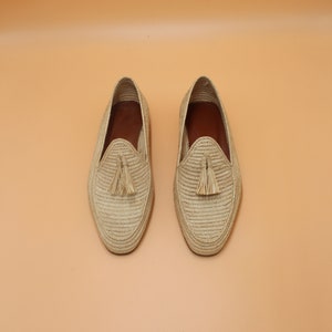 May include: A pair of beige woven leather loafers with tassels. The loafers have a woven texture and a pointed toe.