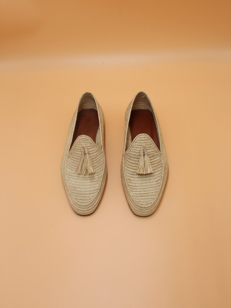 May include: A pair of beige woven leather loafers with tassels. The loafers have a woven texture and a pointed toe.