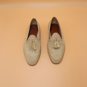 May include: A pair of beige woven leather loafers with tassels. The loafers have a woven texture and a pointed toe.