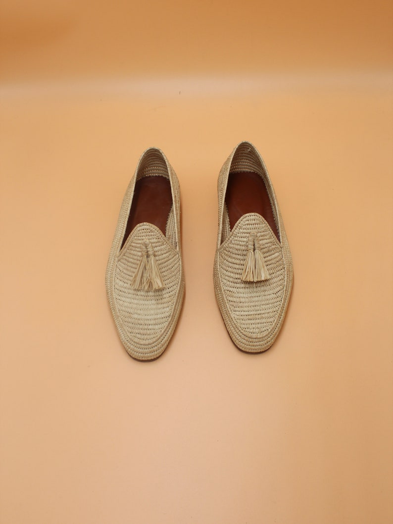 May include: A pair of beige woven leather loafers with tassels. The loafers have a woven texture and a pointed toe.