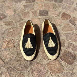 Puede incluir: Un par de zapatos de vestir negros y beige tejidos con un detalle de borla.