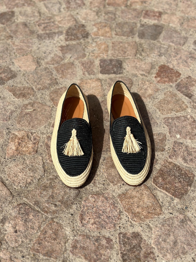 Puede incluir: Un par de zapatos de vestir negros y beige tejidos con un detalle de borla.