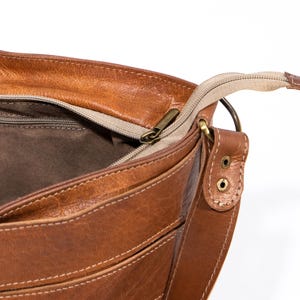 Pu&ograve; includere: Una borsa a tracolla in pelle marrone con chiusura a zip in alto e una tracolla lunga. La borsa ha pi&ugrave; tasche e una fodera marrone.