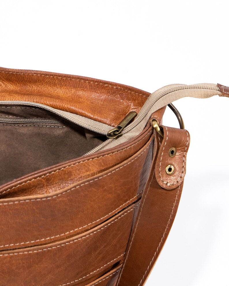 Pu&ograve; includere: Una borsa a tracolla in pelle marrone con chiusura a zip in alto e una tracolla lunga. La borsa ha pi&ugrave; tasche e una fodera marrone.