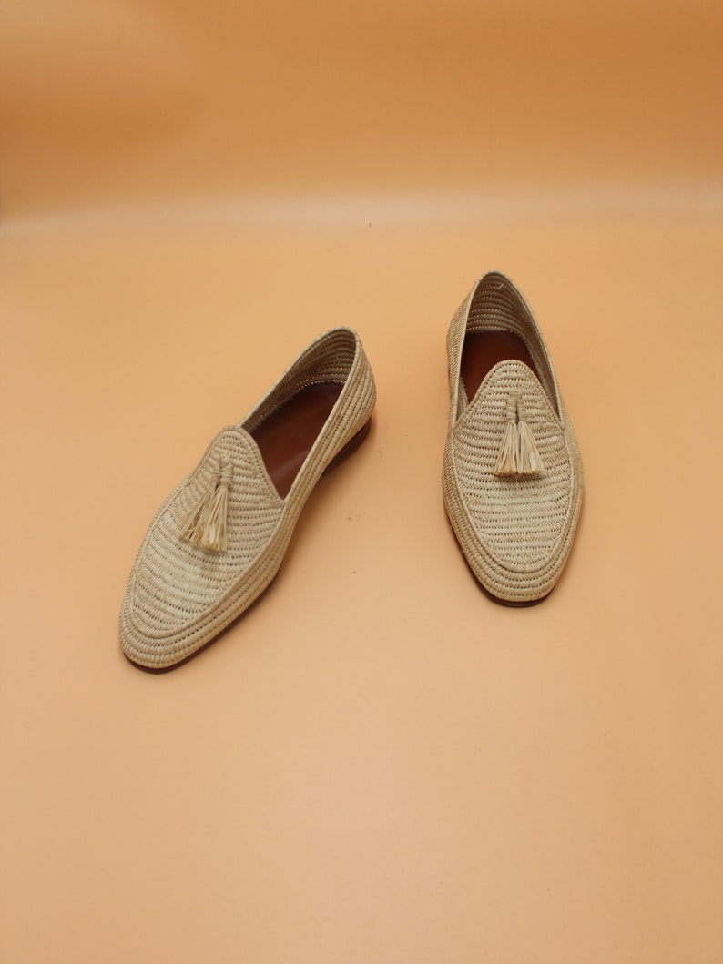May include: A pair of beige woven leather loafers with tassels. The loafers have a pointed toe and a flat sole.