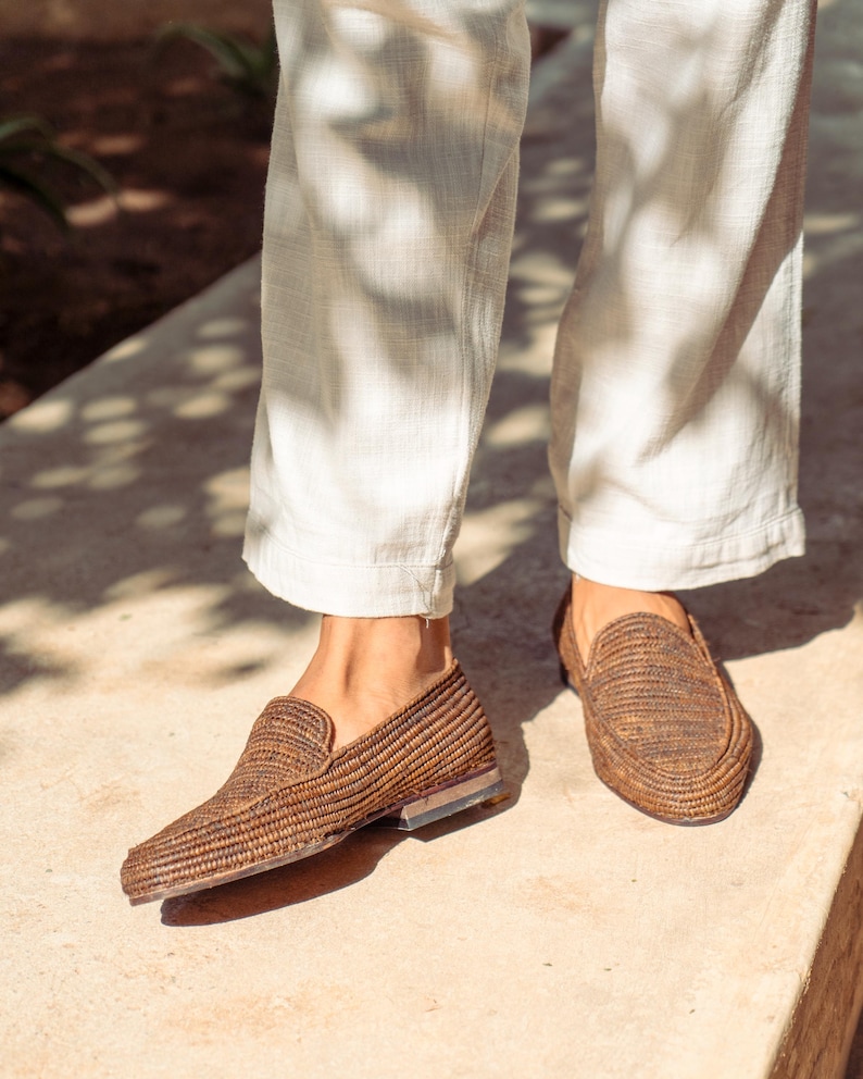 K&ouml;nnte beinhalten: Ein Paar braune geflochtene Lederschuhe mit leicht spitzer Zehenpartie. Die Schuhe werden von einer Person getragen, die eine wei&szlig;e Hose tr&auml;gt.