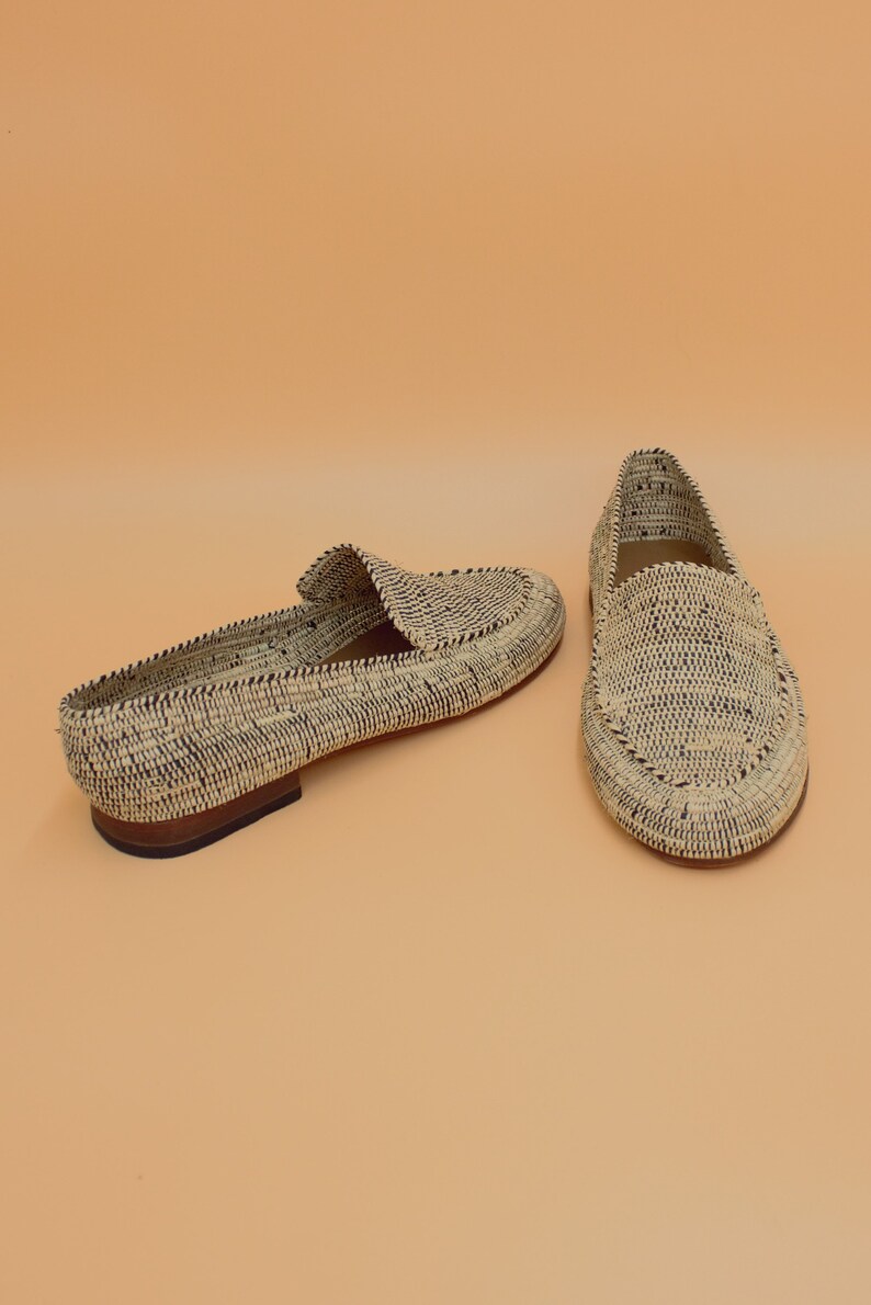 Pode incluir: Um par de mocassins de palha tran&ccedil;ada com acabamento preto. Os mocassins t&ecirc;m uma sola plana e uma ponta pontiaguda.