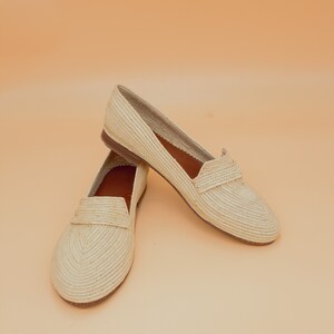 May include: A pair of beige woven leather loafers. The loafers have a pointed toe and a flat sole.