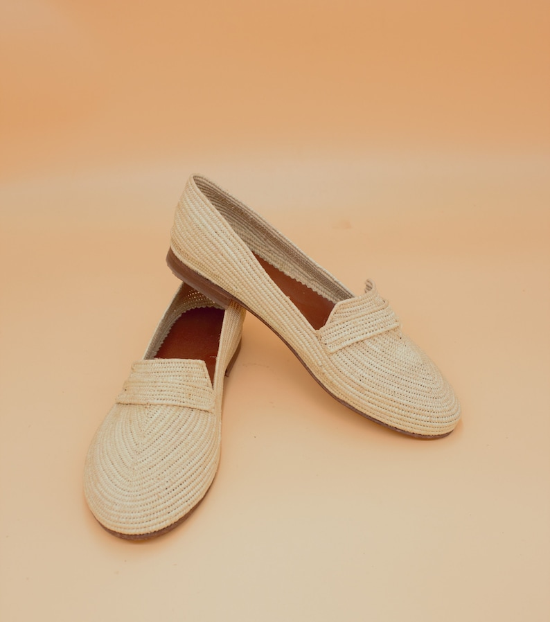 May include: A pair of beige woven leather loafers. The loafers have a pointed toe and a flat sole.