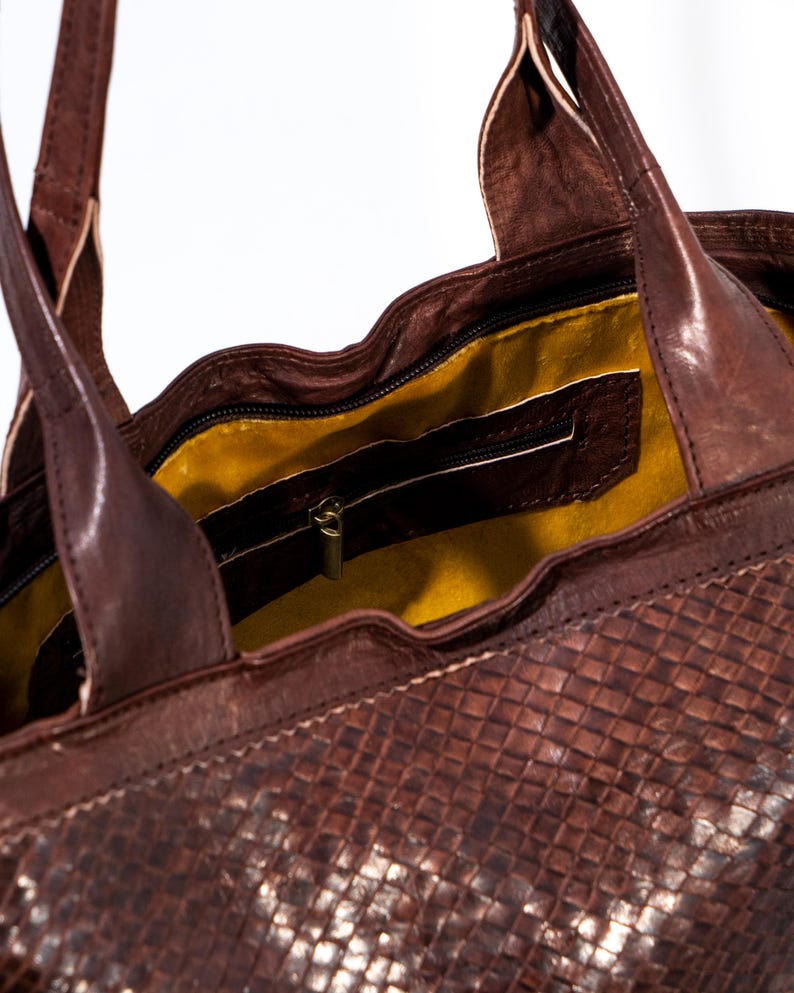 Puede incluir: Un bolso tote de cuero marr&oacute;n con un patr&oacute;n tejido. El bolso tiene un bolsillo con cremallera en el interior y un forro amarillo.