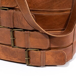 Pu&ograve; includere: Una borsa in pelle marrone con pi&ugrave; fibbie e una lunga tracolla. La borsa &egrave; realizzata in pelle spessa e resistente e ha un aspetto rustico e vintage.