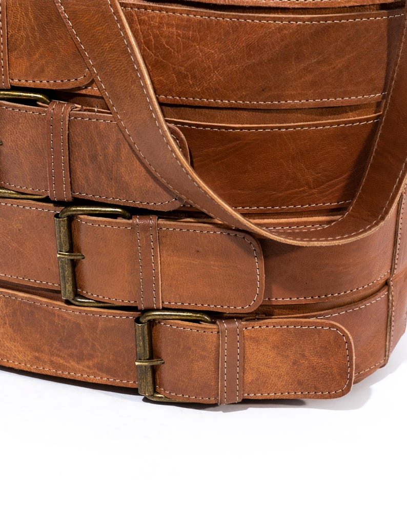 Pu&ograve; includere: Una borsa in pelle marrone con pi&ugrave; fibbie e una lunga tracolla. La borsa &egrave; realizzata in pelle spessa e resistente e ha un aspetto rustico e vintage.