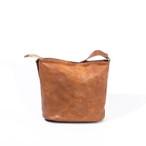 Pu&ograve; includere: Una borsa tote in pelle marrone con un solo cinturino. La borsa ha un aspetto leggermente cascante e un design semplice.