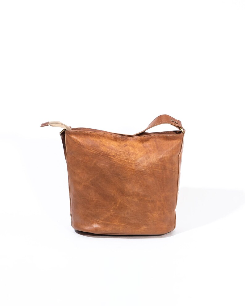 Pu&ograve; includere: Una borsa tote in pelle marrone con un solo cinturino. La borsa ha un aspetto leggermente cascante e un design semplice.